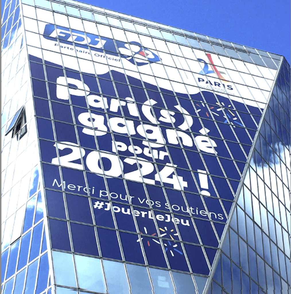 Grand visuel publicitaire bleu et blanc posé sur une façade vitrée.