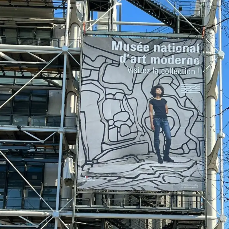 Grande bâche illustrée suspendue sur la façade métallique d’un musée.
