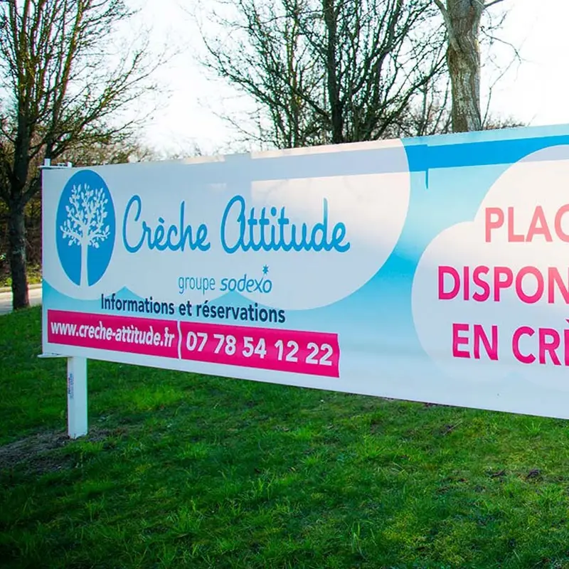 Banderole publicitaire de crèche fixée sur une clôture devant un espace vert.