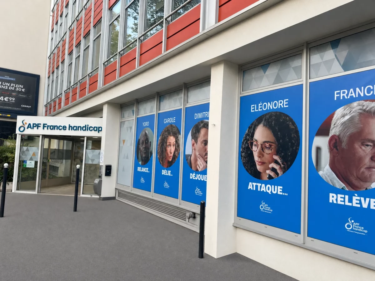 Vue en perspective des bâches bleues et des portraits installés devant les vitrines d’APF France handicap à Paris.