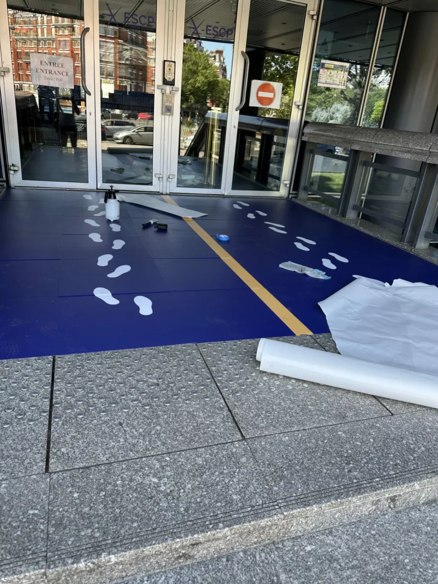 Adhésifs de sol bleus et empreintes blanches guidant les visiteurs à l’entrée.