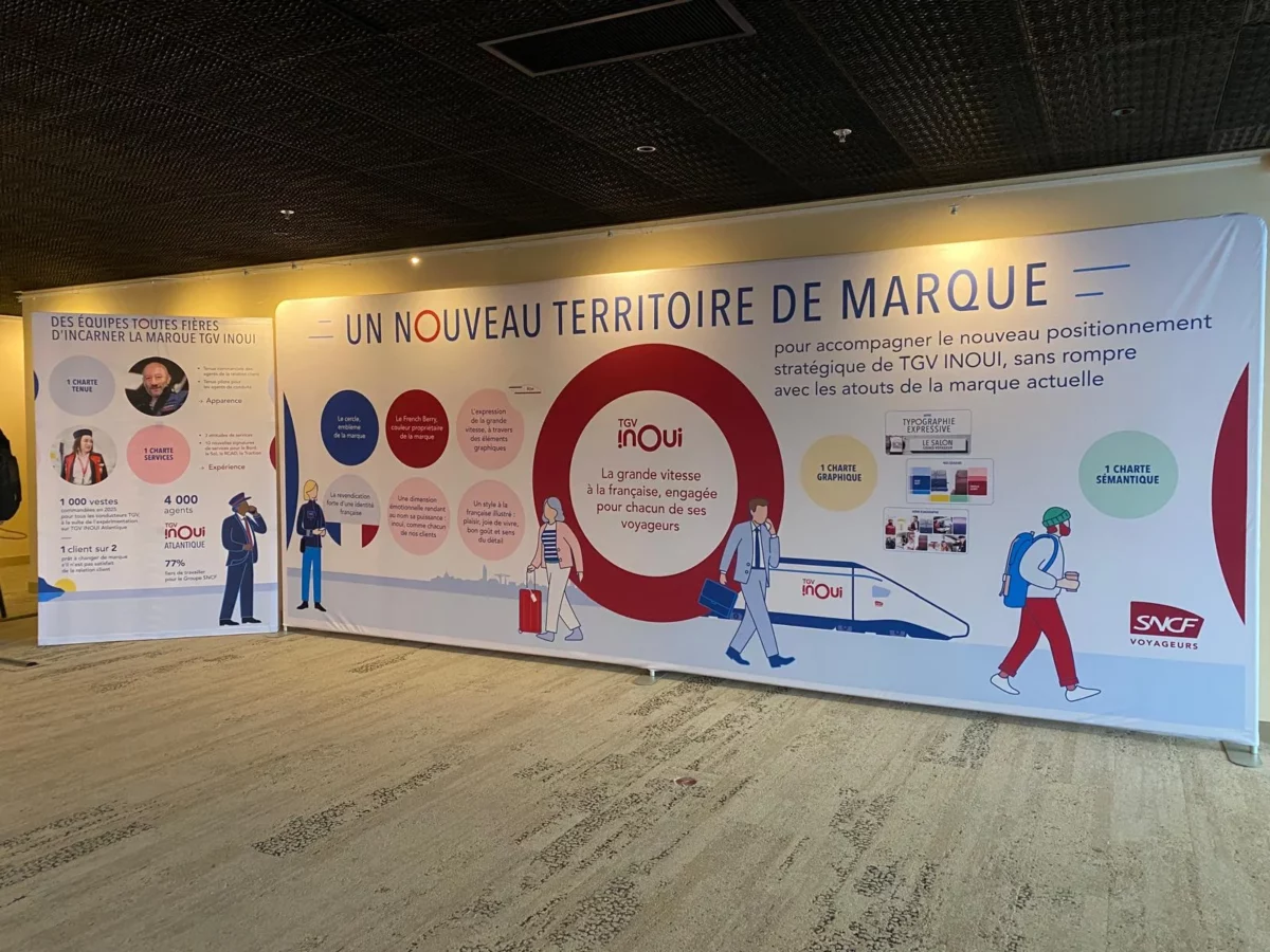 Mur d’image de six mètres de large présentant l’univers de marque TGV INOUI, accompagné d’un support vertical imprimé.